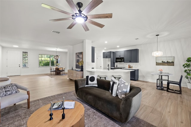 living room with light wood-type flooring, ceiling fan with notable chandelier, and sink