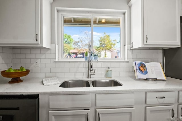 kitchen featuring light stone counters, a sink, white cabinets, black dishwasher, and tasteful backsplash