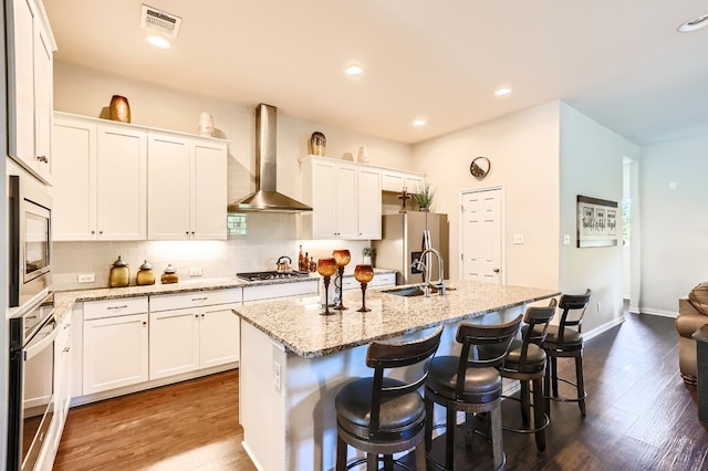 kitchen featuring white cabinetry, wall chimney range hood, hardwood / wood-style flooring, and a kitchen island with sink