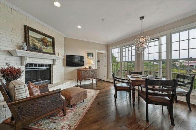 dining space featuring dark wood-type flooring, brick wall, a chandelier, a fireplace, and ornamental molding