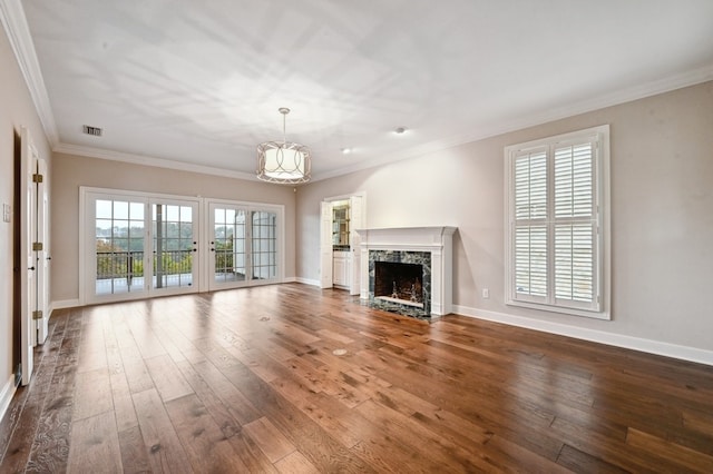 unfurnished living room featuring a high end fireplace, wood-type flooring, an inviting chandelier, and ornamental molding