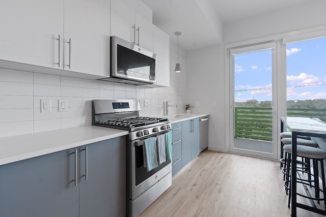 kitchen with white cabinets, appliances with stainless steel finishes, hanging light fixtures, light countertops, and light wood-type flooring