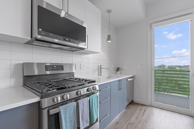 kitchen with appliances with stainless steel finishes, light countertops, a sink, and pendant lighting