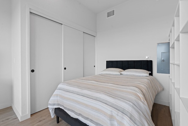 bedroom featuring a closet, visible vents, light wood-style floors, electric panel, and baseboards