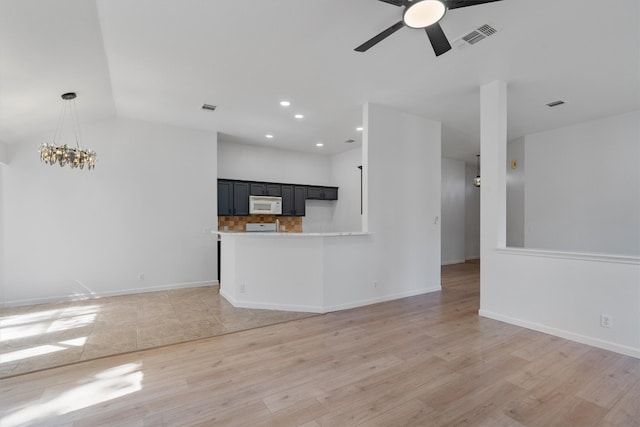 unfurnished living room featuring ceiling fan with notable chandelier and light hardwood / wood-style flooring