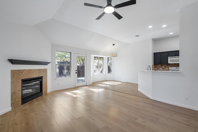 unfurnished living room with lofted ceiling, a tile fireplace, ceiling fan, and light hardwood / wood-style flooring