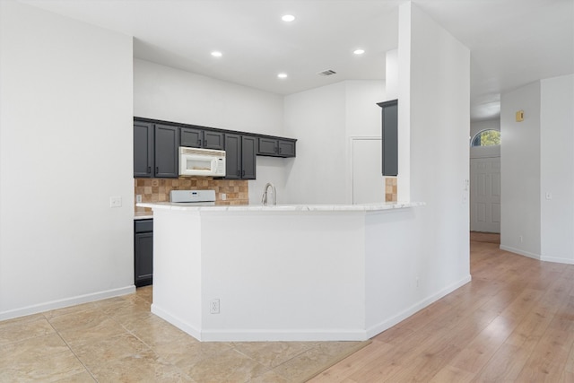 kitchen featuring kitchen peninsula, sink, backsplash, light wood-type flooring, and white appliances