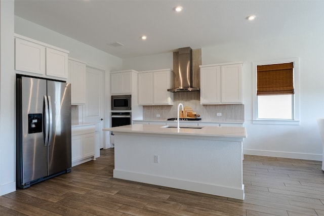 kitchen with stainless steel appliances, a center island with sink, wall chimney exhaust hood, dark hardwood / wood-style floors, and white cabinetry