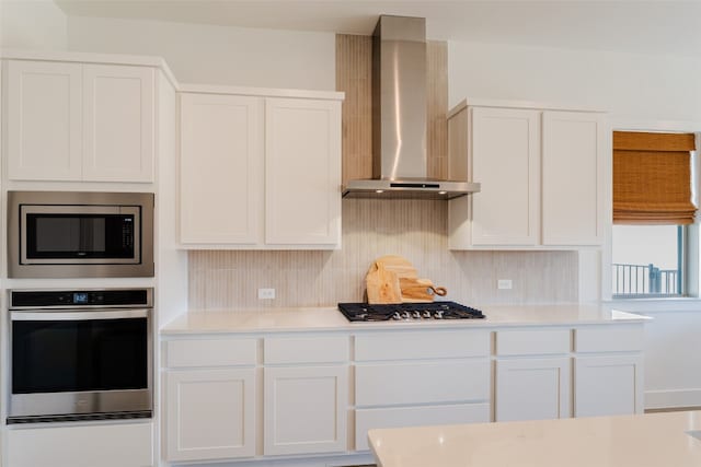 kitchen featuring white cabinetry, decorative backsplash, appliances with stainless steel finishes, and wall chimney range hood