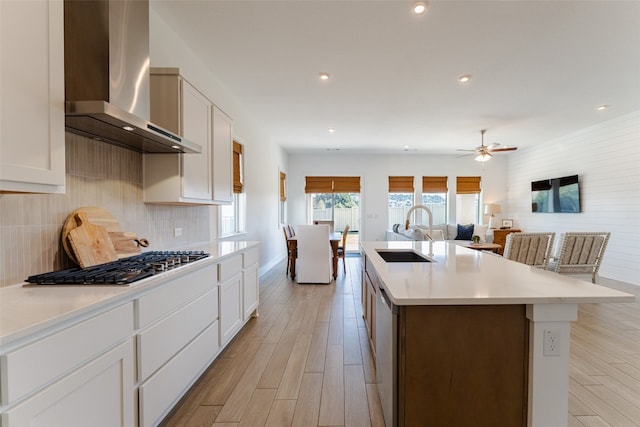 kitchen with a center island with sink, white cabinetry, sink, wall chimney exhaust hood, and light hardwood / wood-style flooring