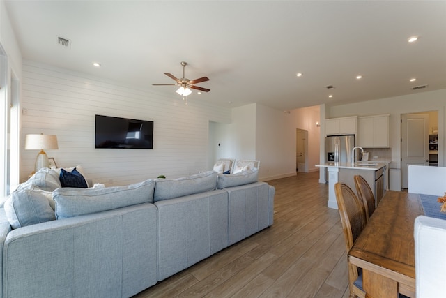 living room with light hardwood / wood-style floors, ceiling fan, and sink