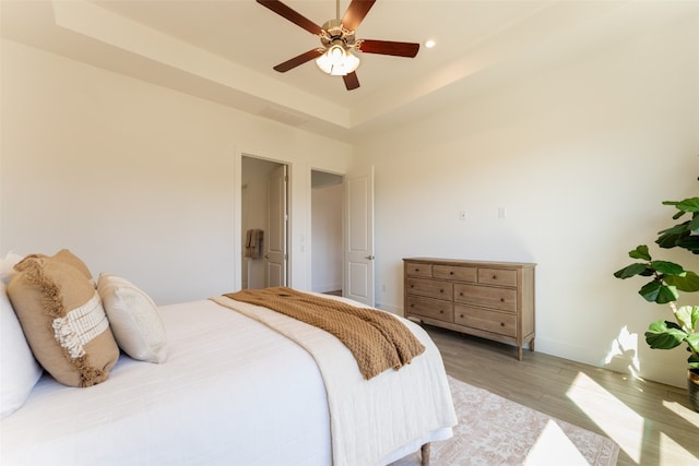 bedroom with hardwood / wood-style flooring, ceiling fan, and a tray ceiling