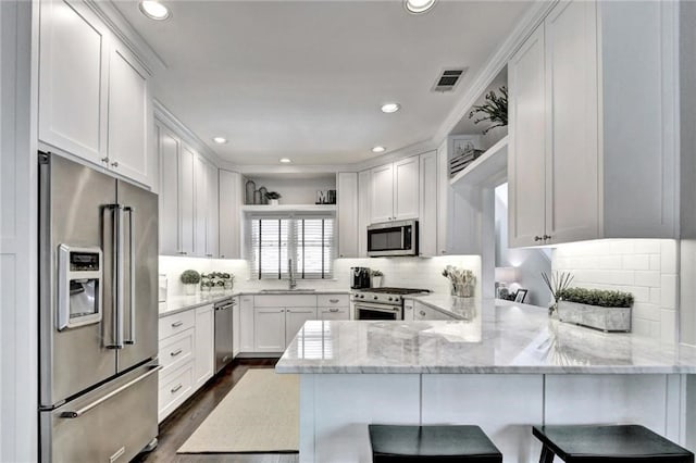 kitchen featuring visible vents, white cabinets, a sink, high quality appliances, and a peninsula