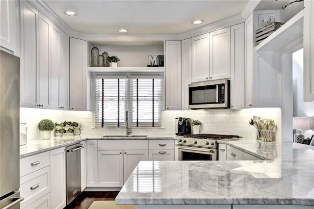 kitchen with a peninsula, a sink, white cabinets, appliances with stainless steel finishes, and tasteful backsplash