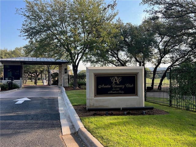 community sign with driveway, fence, and a lawn