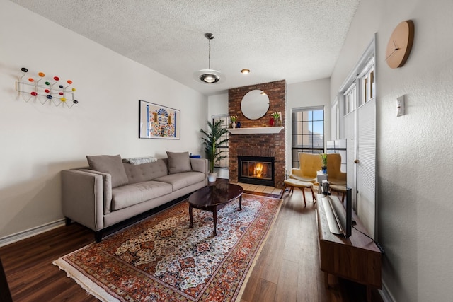 living room featuring dark wood-type flooring, a textured ceiling, and a brick fireplace