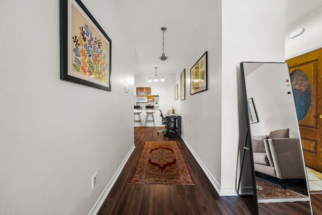 corridor with dark wood-type flooring, a textured ceiling, and a notable chandelier