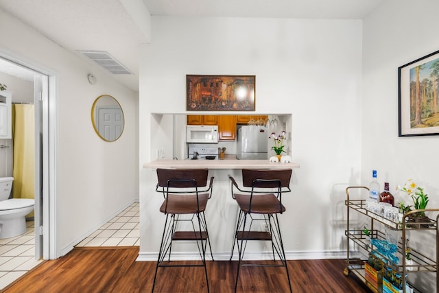 3001 Cedar St Unit 310, Austin, TX 78705 - kitchen featuring white appliances, a kitchen breakfast bar, light countertops, brown cabinetry, and wood finished floors