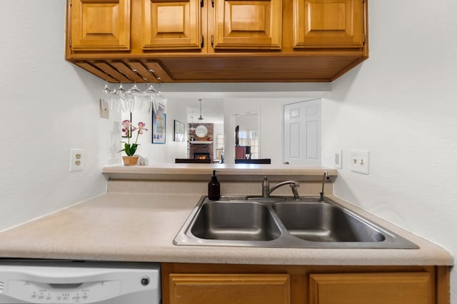 kitchen with white dishwasher, sink, and a brick fireplace