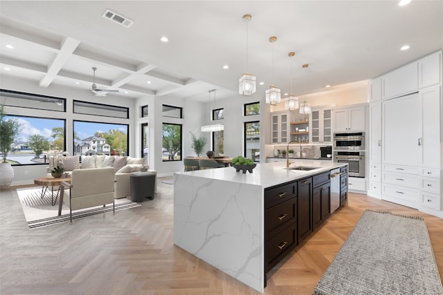 kitchen with white cabinets, an island with sink, coffered ceiling, beam ceiling, and pendant lighting