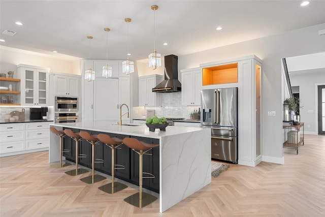 kitchen featuring a kitchen island with sink, appliances with stainless steel finishes, wall chimney exhaust hood, and white cabinets