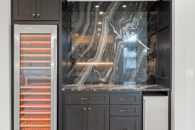 bar with dark stone counters, beverage cooler, and stainless steel fridge