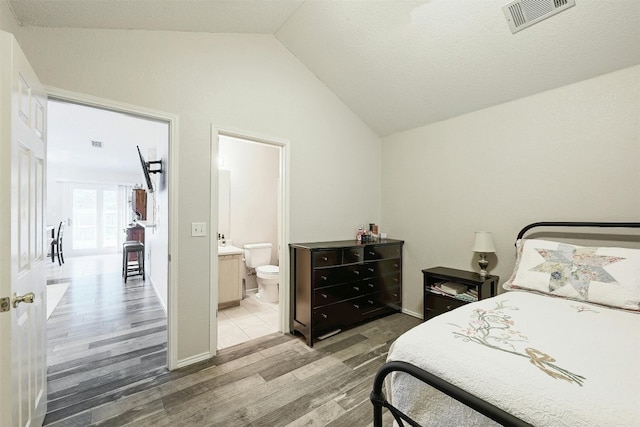 bedroom with lofted ceiling, hardwood / wood-style floors, and connected bathroom