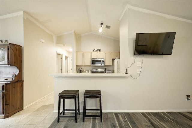 kitchen featuring light tile patterned floors, a breakfast bar, appliances with stainless steel finishes, light brown cabinetry, and vaulted ceiling