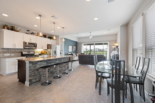 kitchen with light stone counters, white cabinetry, appliances with stainless steel finishes, decorative light fixtures, and an island with sink