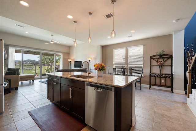 kitchen with sink, appliances with stainless steel finishes, light stone countertops, an island with sink, and pendant lighting