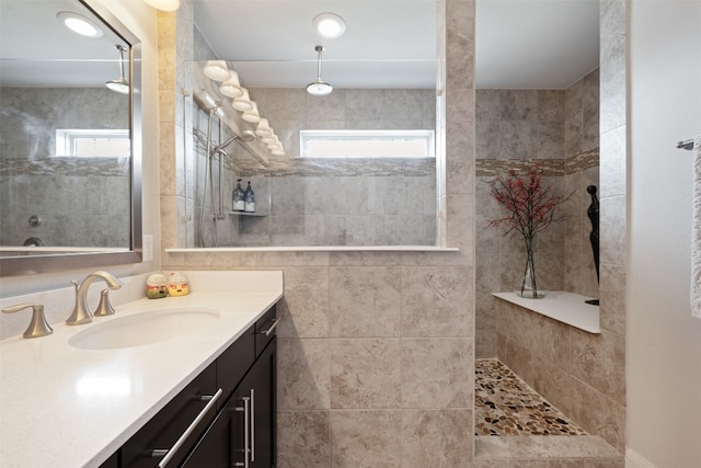 bathroom with tiled shower, vanity, and a healthy amount of sunlight