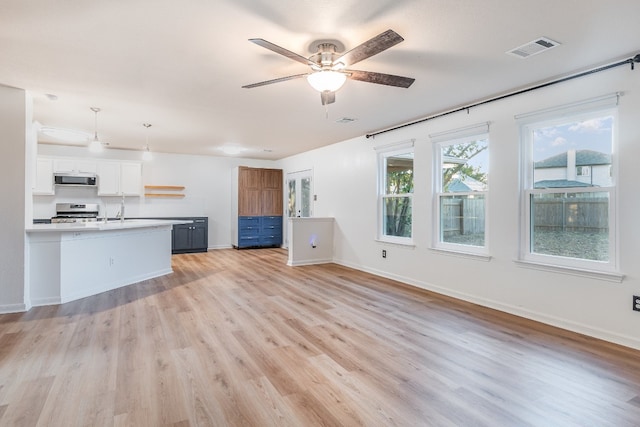 kitchen featuring a center island with sink, white cabinets, hanging light fixtures, range, and light hardwood / wood-style flooring