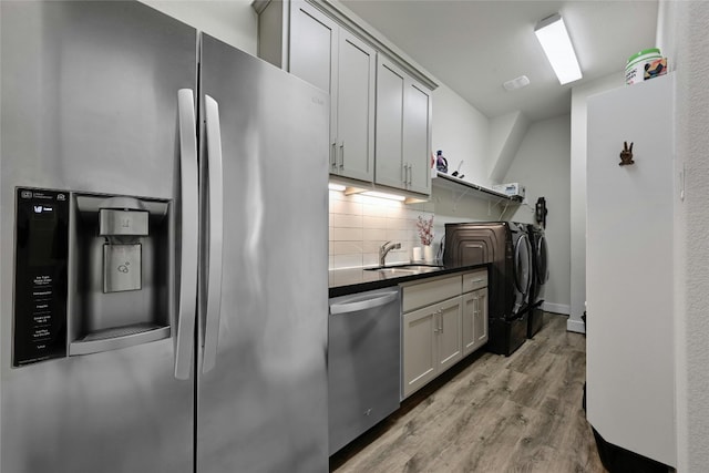 kitchen with stainless steel appliances, gray cabinets, sink, washing machine and dryer, and light hardwood / wood-style flooring