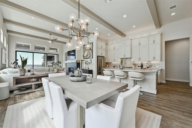 dining room with beamed ceiling, sink, a notable chandelier, and light wood-type flooring