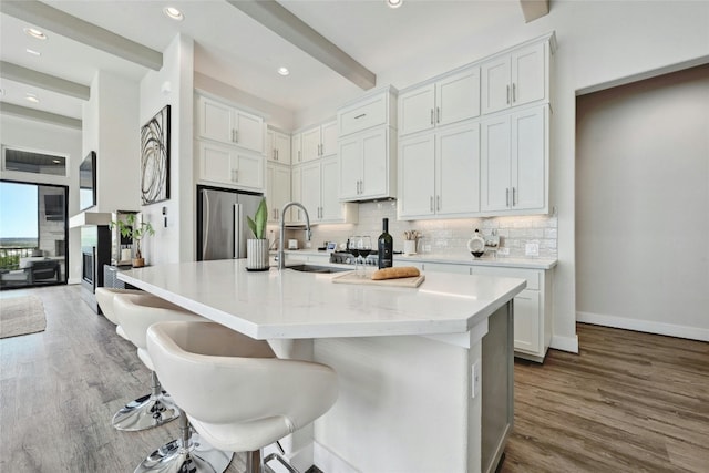 kitchen with sink, a kitchen bar, dark hardwood / wood-style floors, white cabinets, and stainless steel fridge