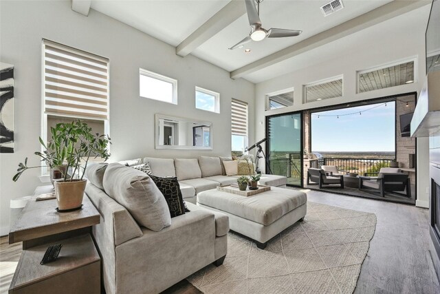 living room featuring a towering ceiling, light hardwood / wood-style floors, beamed ceiling, and ceiling fan