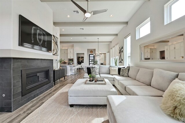 living room featuring hardwood / wood-style floors, a tile fireplace, ceiling fan, and beam ceiling