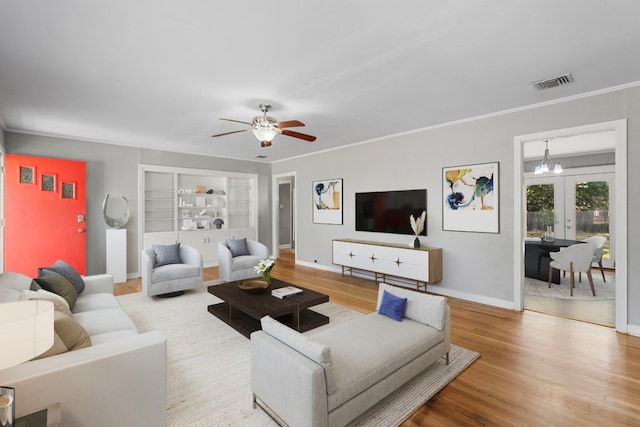 living room with french doors, ceiling fan with notable chandelier, light hardwood / wood-style flooring, and ornamental molding