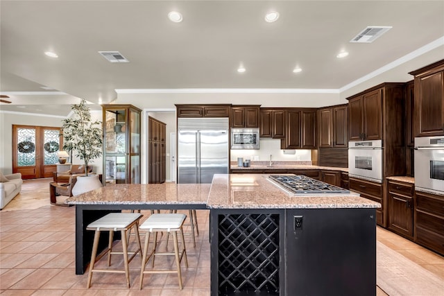 kitchen featuring built in appliances, a breakfast bar area, dark brown cabinets, light stone countertops, and a spacious island