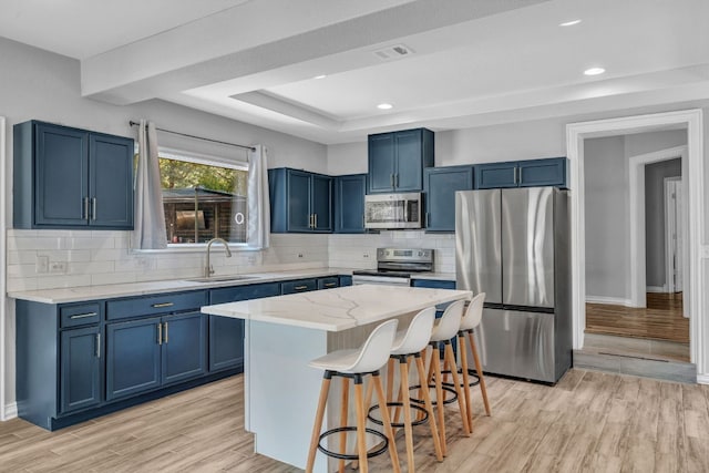 kitchen with sink, a center island, appliances with stainless steel finishes, a kitchen breakfast bar, and a raised ceiling