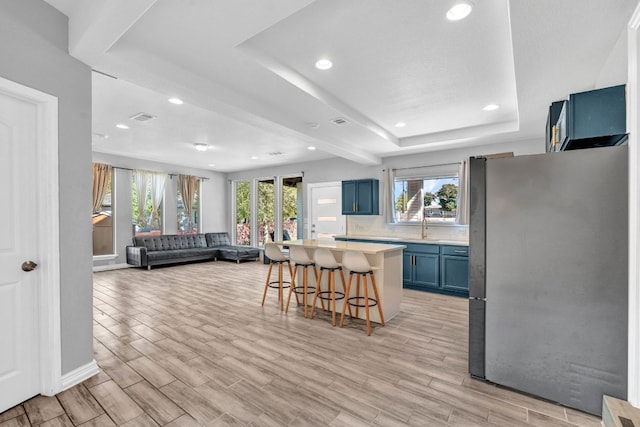 kitchen with stainless steel refrigerator, blue cabinets, a breakfast bar area, a center island, and a raised ceiling