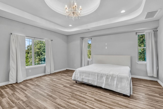 bedroom featuring a notable chandelier, a tray ceiling, and light wood-type flooring