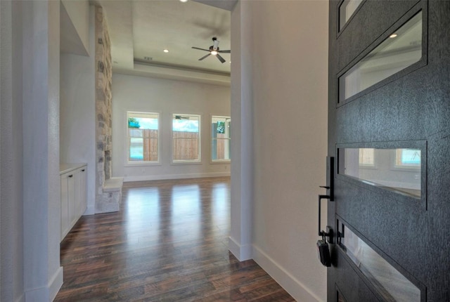 interior space featuring a tray ceiling, dark wood-type flooring, and baseboards