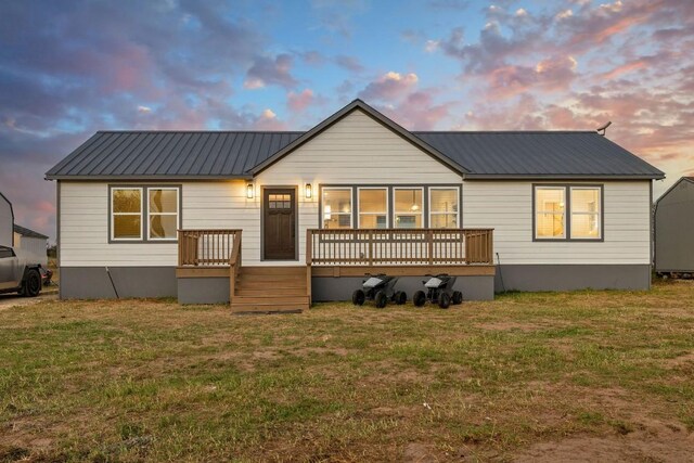 back house at dusk with a lawn and a deck