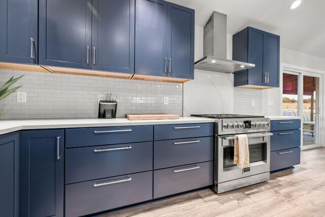 kitchen featuring backsplash, range with two ovens, light hardwood / wood-style floors, blue cabinets, and wall chimney exhaust hood