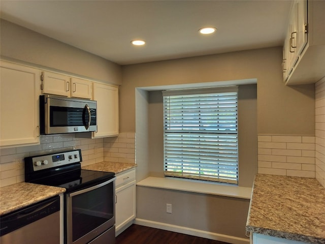 kitchen featuring decorative backsplash, appliances with stainless steel finishes, dark hardwood / wood-style flooring, light stone countertops, and white cabinets