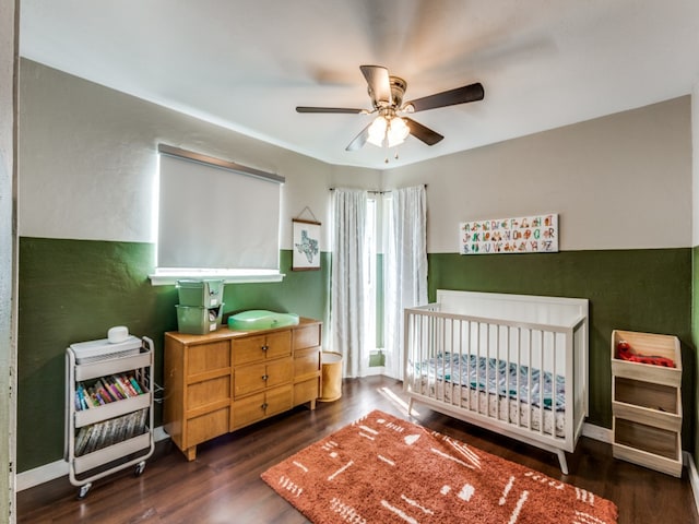 bedroom with dark hardwood / wood-style flooring, a nursery area, and ceiling fan