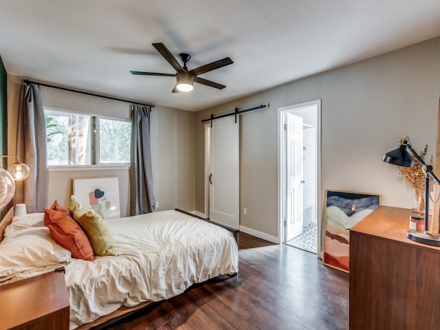 bedroom with a barn door, ensuite bath, ceiling fan, and dark hardwood / wood-style floors