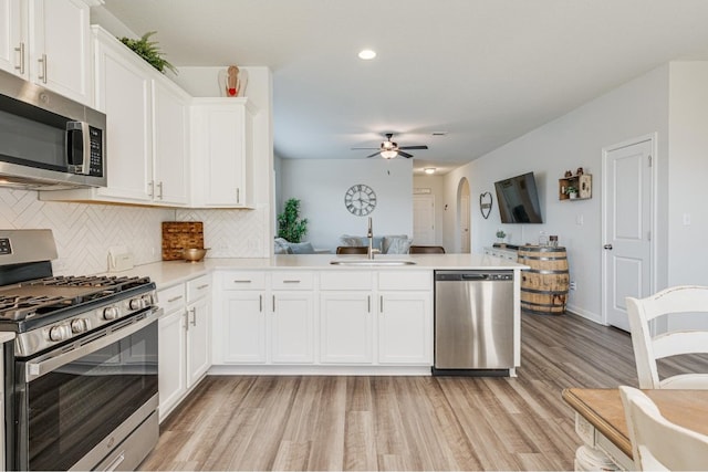 kitchen with kitchen peninsula, stainless steel appliances, white cabinetry, and light hardwood / wood-style floors