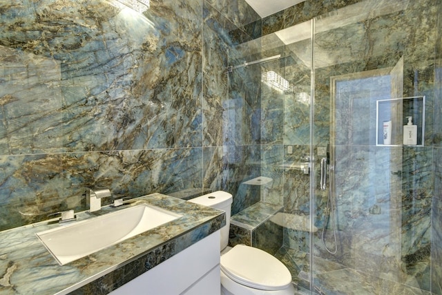 bathroom with tile walls, vanity, toilet, and a shower with shower door